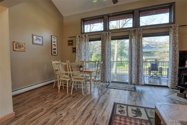 dining room featuring a baseboard radiator, wood finished floors, plenty of natural light, and high vaulted ceiling