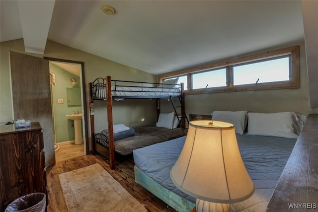 bedroom with wood finished floors, a sink, connected bathroom, and vaulted ceiling