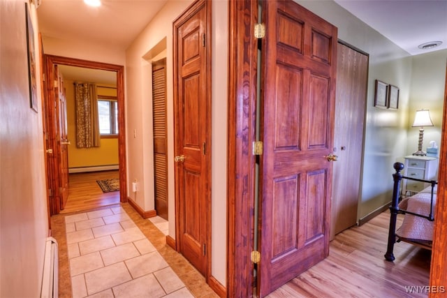 hall featuring baseboards, visible vents, light tile patterned floors, and a baseboard radiator