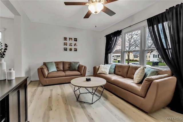 living area featuring a ceiling fan, baseboards, and light wood-style floors