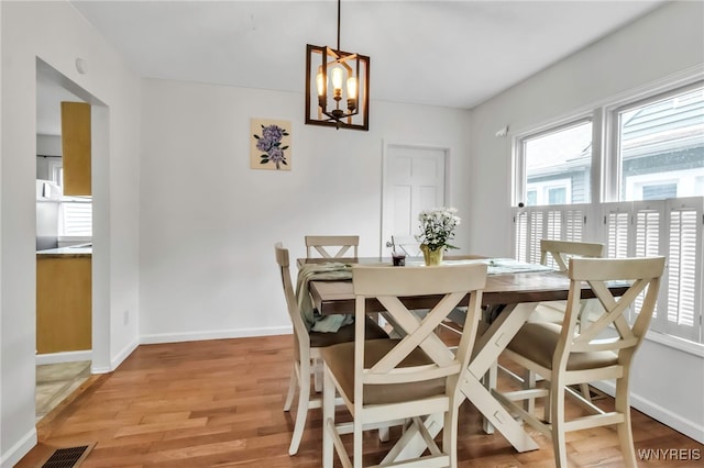dining space with light wood finished floors, an inviting chandelier, visible vents, and baseboards