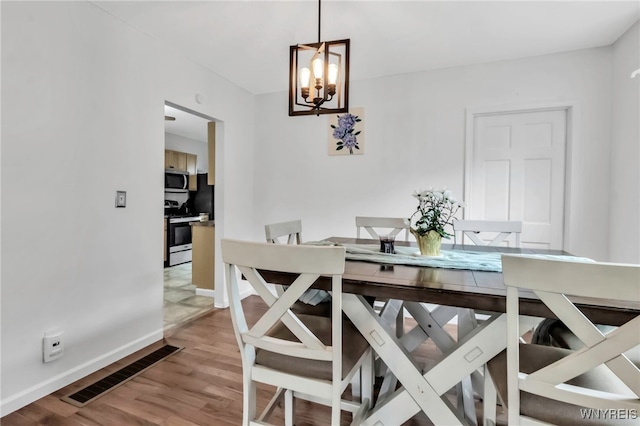 dining space with a notable chandelier, visible vents, wood finished floors, and baseboards