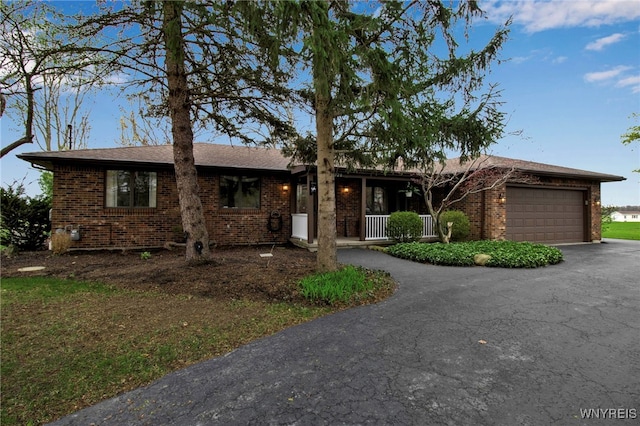 ranch-style house featuring a garage, brick siding, a porch, and aphalt driveway