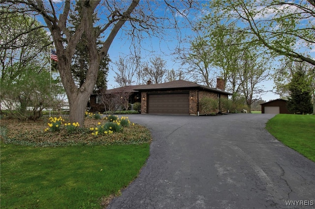 view of front of house featuring a front lawn, a garage, a chimney, driveway, and brick siding