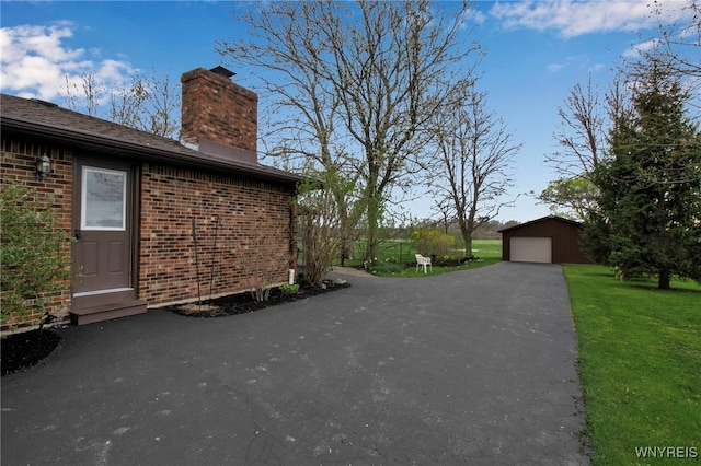 view of property exterior with an outdoor structure, a chimney, a lawn, brick siding, and a garage