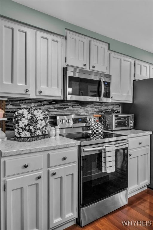 kitchen with tasteful backsplash, white cabinets, appliances with stainless steel finishes, and light stone counters