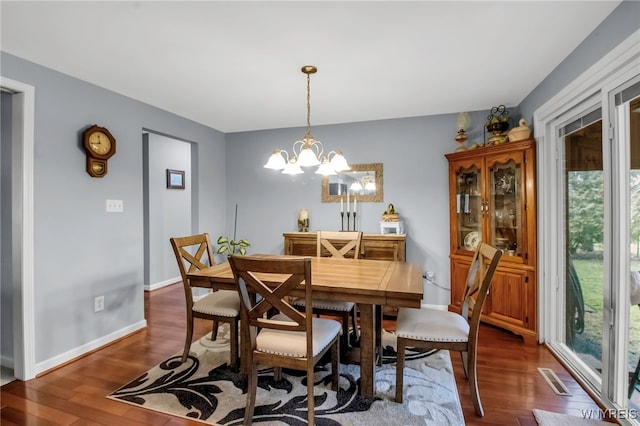 dining room with dark wood-type flooring, a notable chandelier, and baseboards