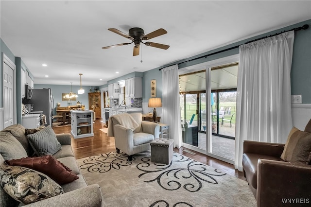 living room with recessed lighting, wood finished floors, and ceiling fan with notable chandelier