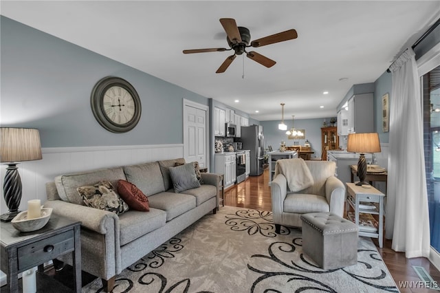 living room with wood finished floors, a wainscoted wall, recessed lighting, and ceiling fan with notable chandelier