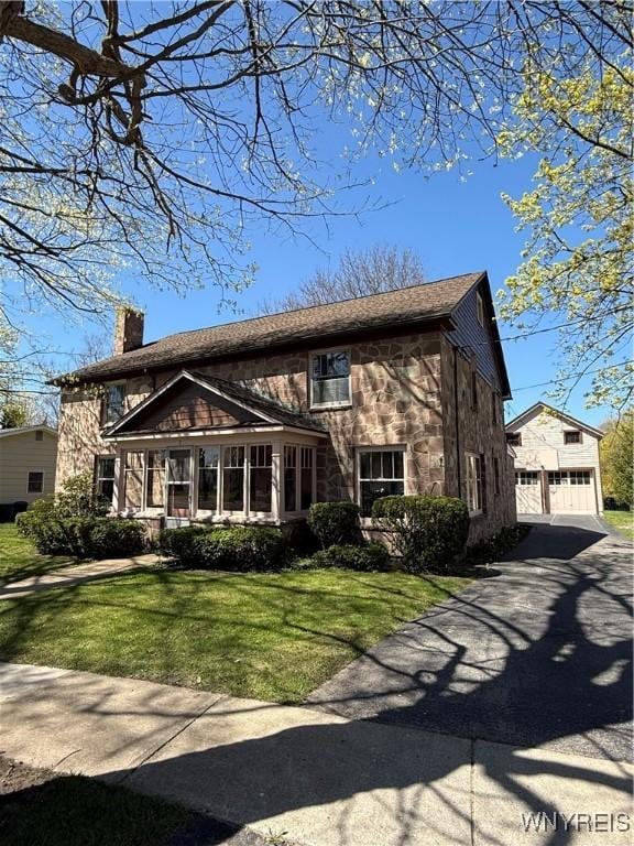 traditional-style house featuring a front yard, a garage, an outdoor structure, stone siding, and a chimney
