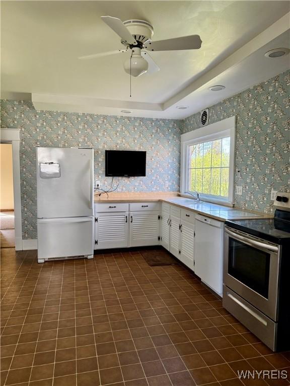kitchen with wallpapered walls, white appliances, white cabinets, and a sink