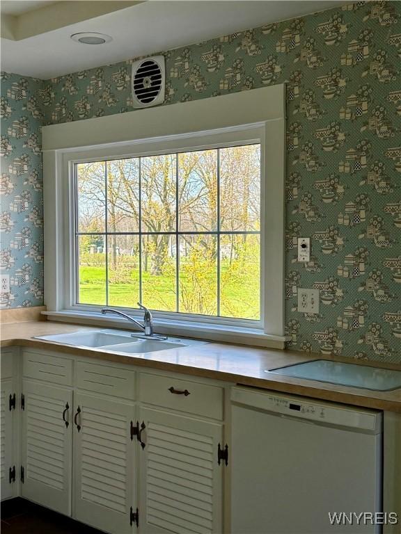 kitchen featuring white cabinetry, a sink, light countertops, wallpapered walls, and white dishwasher