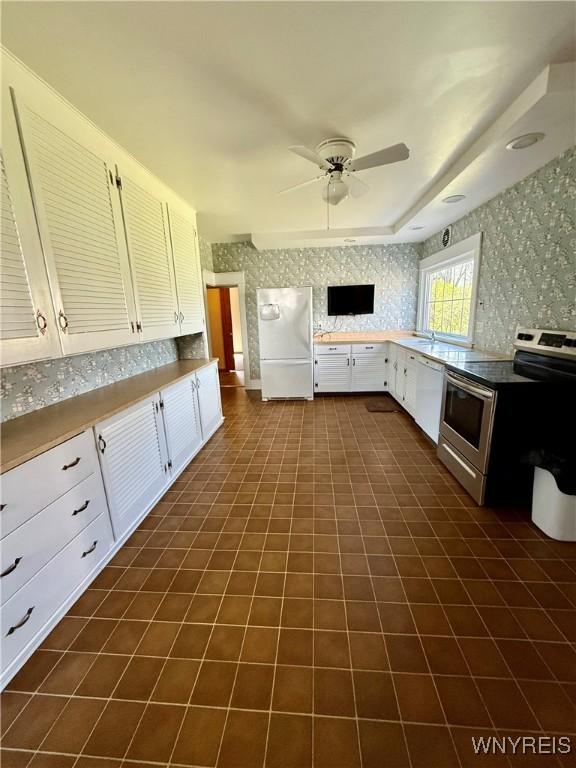 kitchen with dark tile patterned floors, ceiling fan, white cabinetry, white appliances, and wallpapered walls