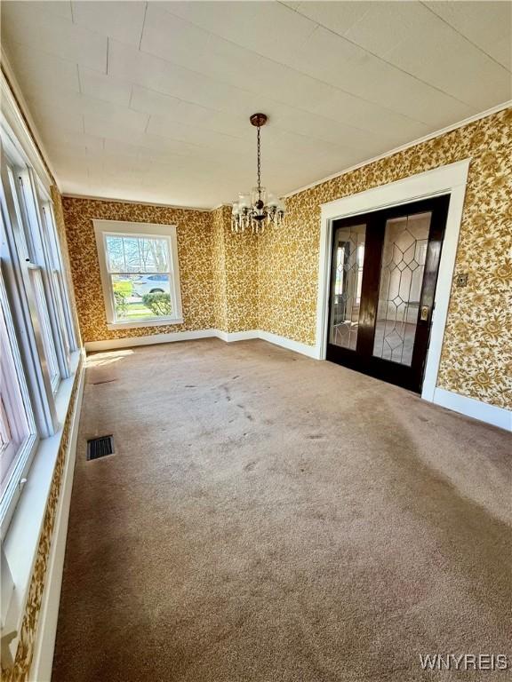 unfurnished dining area featuring a notable chandelier, visible vents, wallpapered walls, and carpet floors