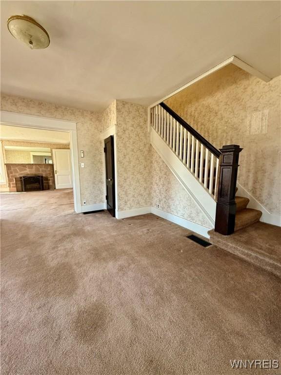 unfurnished living room with carpet, stairway, wallpapered walls, and baseboards