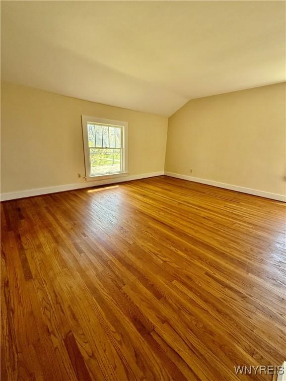 spare room with wood finished floors, vaulted ceiling, and baseboards