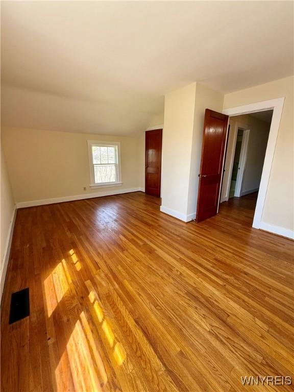 empty room featuring light wood finished floors, visible vents, lofted ceiling, and baseboards