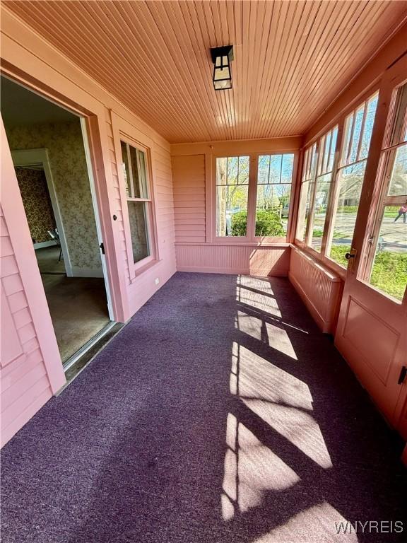 unfurnished sunroom with carpet flooring and wooden ceiling