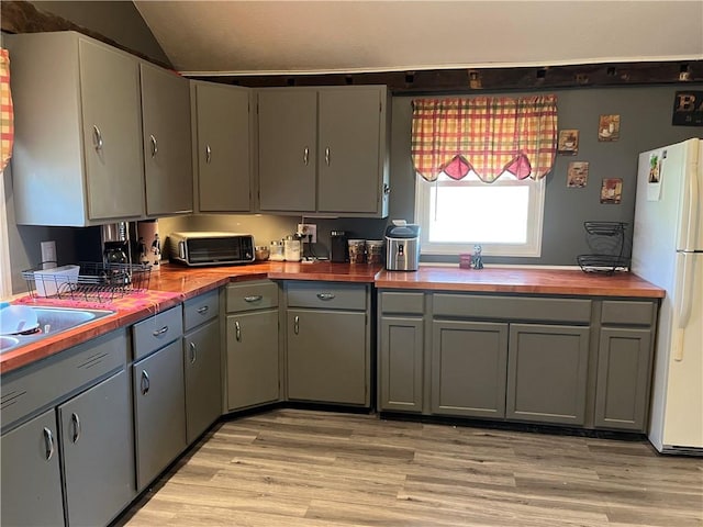 kitchen with freestanding refrigerator, wood counters, light wood finished floors, gray cabinetry, and lofted ceiling