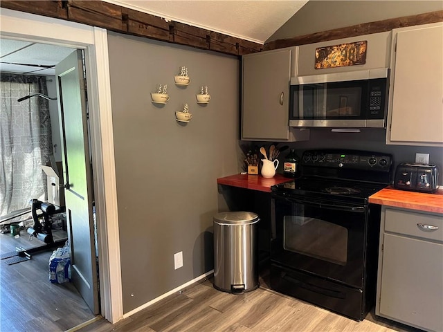 kitchen with stainless steel microwave, light wood-style flooring, electric range, butcher block countertops, and vaulted ceiling
