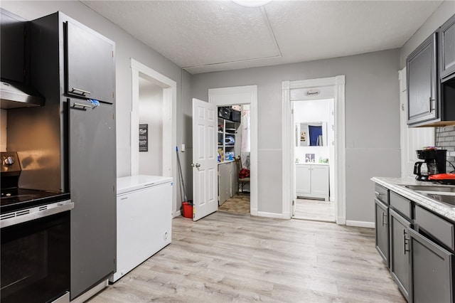 kitchen with a textured ceiling, stainless steel range with electric stovetop, light countertops, light wood finished floors, and refrigerator