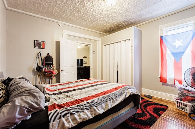bedroom with an ornate ceiling, wood finished floors, a closet, and baseboards