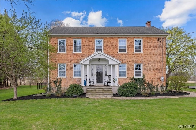 colonial home with a chimney, a front yard, and brick siding