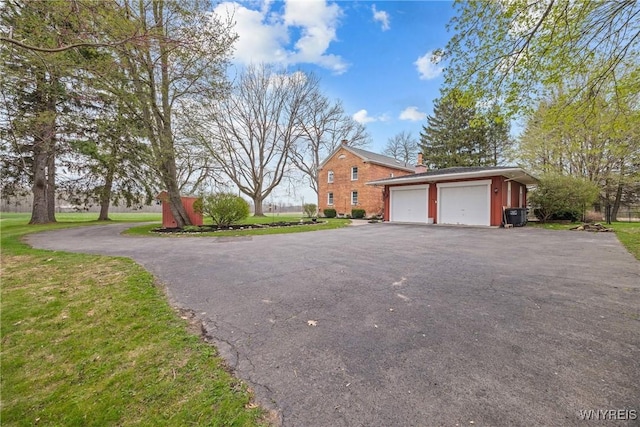 view of side of home featuring a chimney, aphalt driveway, an outbuilding, and a yard