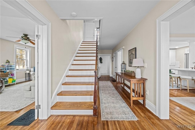stairway with baseboards, wood finished floors, and a ceiling fan