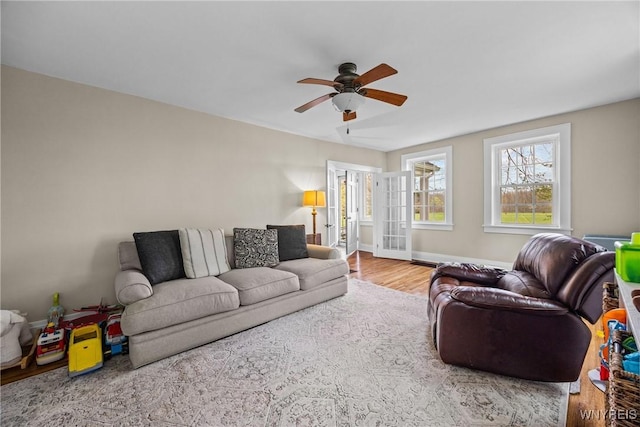 living area with wood finished floors, french doors, a ceiling fan, and baseboards