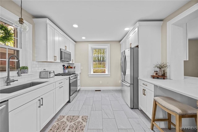 kitchen with white cabinets, a sink, stainless steel appliances, light countertops, and baseboards