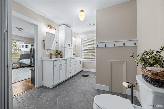 ensuite bathroom with ensuite bath, double vanity, toilet, baseboards, and visible vents