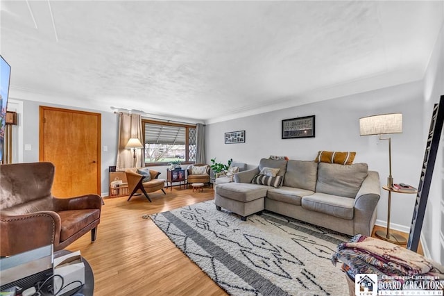living area with crown molding, baseboards, and light wood-type flooring