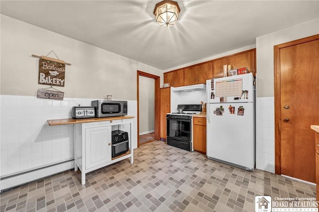 kitchen featuring freestanding refrigerator, baseboard heating, stainless steel microwave, under cabinet range hood, and range with gas cooktop