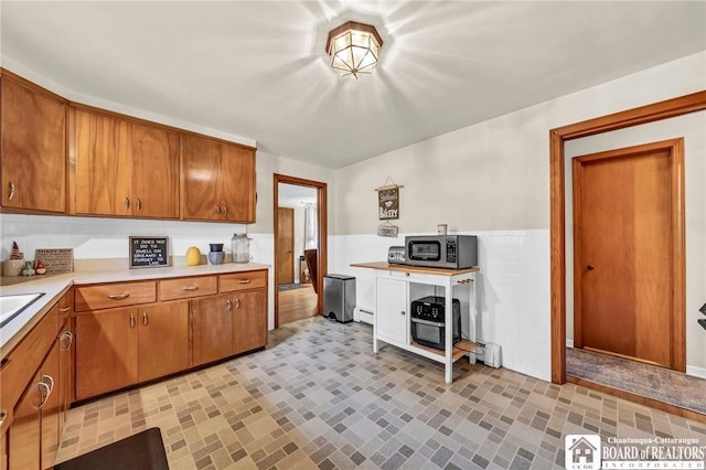 kitchen featuring baseboard heating, wainscoting, brown cabinets, light countertops, and stainless steel microwave