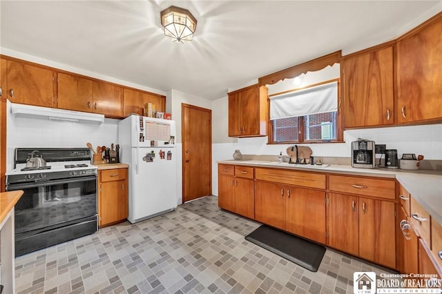 kitchen featuring freestanding refrigerator, gas range oven, light countertops, under cabinet range hood, and a sink