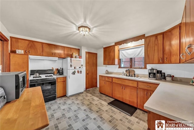 kitchen with a sink, freestanding refrigerator, stainless steel microwave, gas range, and under cabinet range hood
