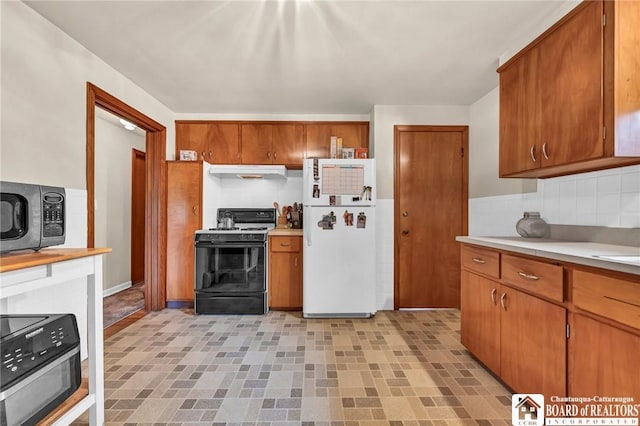kitchen with freestanding refrigerator, black microwave, light countertops, under cabinet range hood, and gas stove