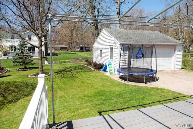 view of yard featuring a detached garage, a trampoline, an outdoor structure, and driveway