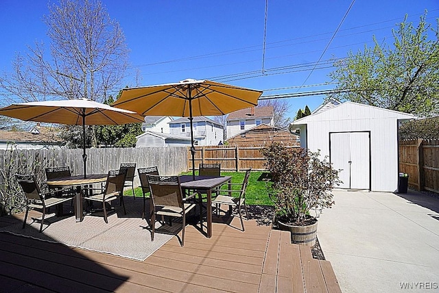 wooden terrace with a storage unit, a fenced backyard, an outbuilding, and outdoor dining space