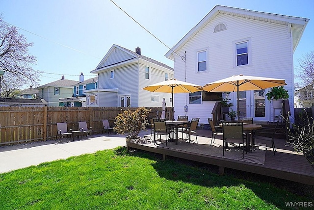 back of property featuring a lawn, outdoor dining area, fence, and a wooden deck