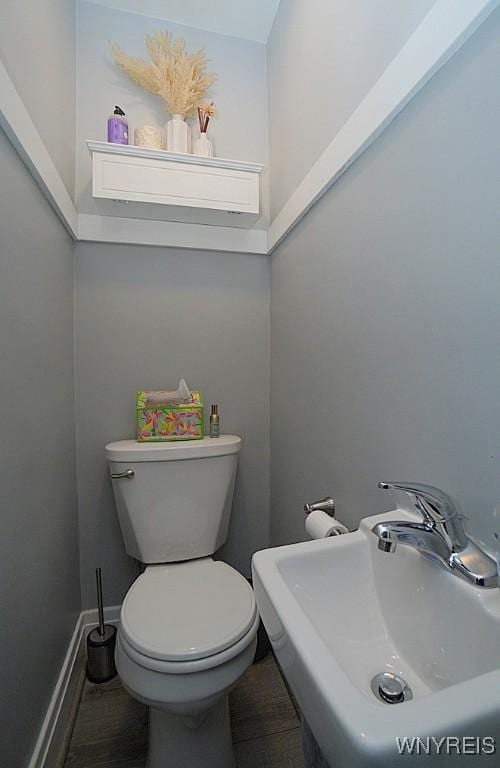 half bathroom featuring toilet, baseboards, and a sink