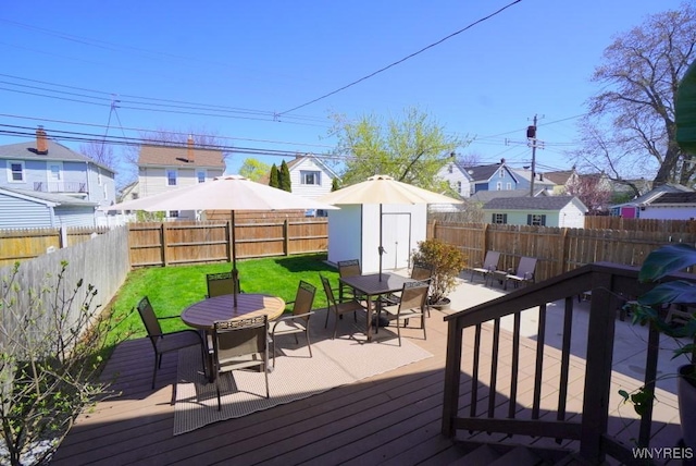 deck with an outdoor structure, outdoor dining area, a fenced backyard, a storage unit, and a residential view