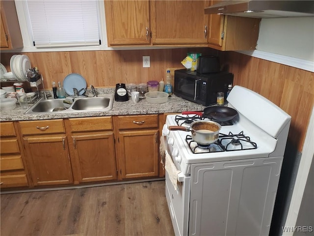 kitchen featuring a sink, black microwave, white gas stove, range hood, and brown cabinetry