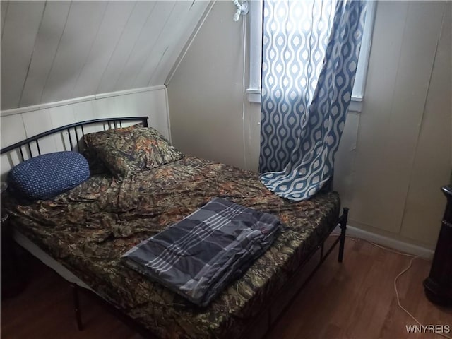 bedroom featuring a decorative wall, vaulted ceiling, and wood finished floors