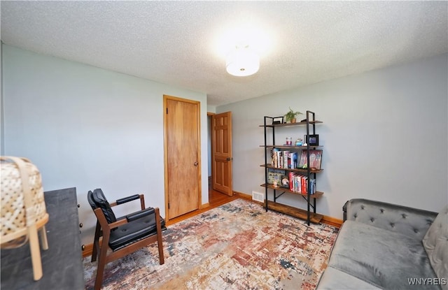 living area with baseboards, visible vents, wood finished floors, and a textured ceiling