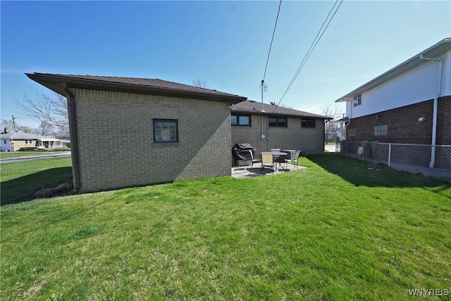 rear view of property featuring fence, a lawn, a patio area, and brick siding