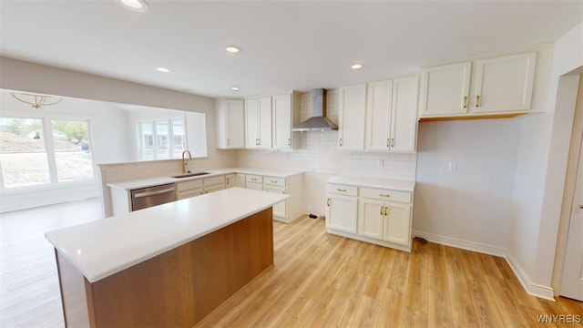 kitchen with tasteful backsplash, light wood-style floors, dishwasher, a sink, and wall chimney exhaust hood