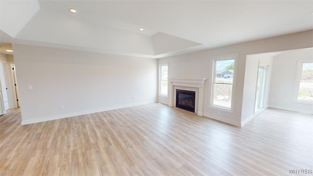 unfurnished living room with a raised ceiling, baseboards, a glass covered fireplace, light wood-type flooring, and recessed lighting