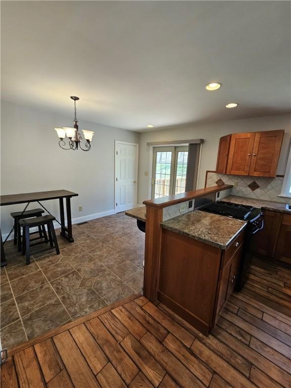 kitchen with range with gas stovetop, an inviting chandelier, dark wood-style flooring, a peninsula, and backsplash